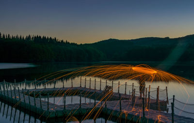 Man spinning wire wool on pier in lake against clear sky at sunset