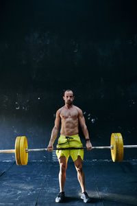 Shirtless fit young man working out with horizontal bar at indoors gym