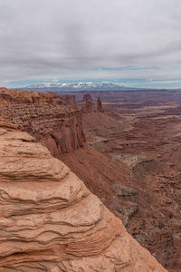 Full frame view of sandstone cliffs with a rugged canyon valley and snow capped mountains