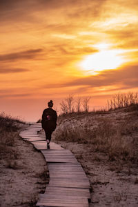 Rear view of man on footpath against sky during sunset