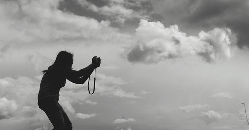 Low angle view woman photographing through camera against cloudy sky