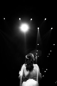 Rear view of woman standing against illuminated lights at night