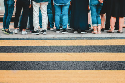 Low section of people standing by zebra crossing on road