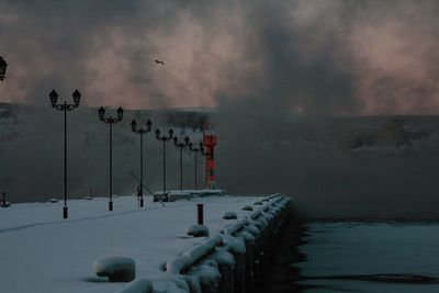 Snow covered pier on sea against cloudy sky at dusk