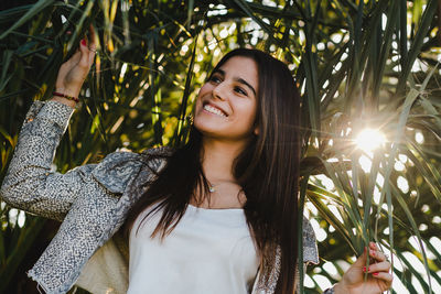 Smiling young woman looking away while standing against plants