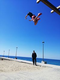 Full length of man jumping on beach against clear blue sky