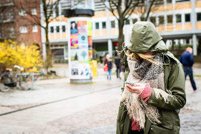 Woman in raincoat using mobile phone on street