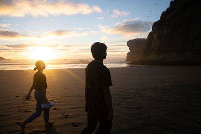 Men on beach against sky during sunset