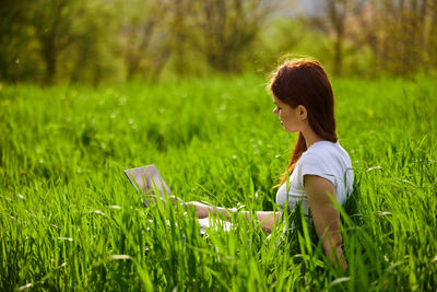 Side view of young woman sitting on grassy field