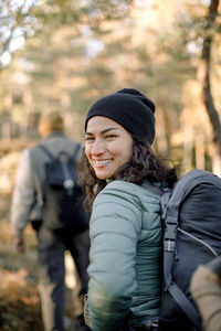 Happy woman looking over shoulder while hiking in forest