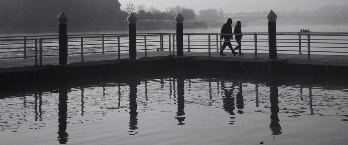 water, sea, railing, silhouette, pier, men, reflection, built structure, sky, bridge - man made structure, lifestyles, waterfront, architecture, connection, walking, leisure activity, person, river