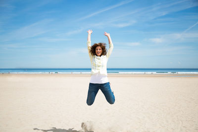 Full length of woman jumping in mid-air at beach against sky
