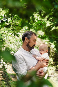 Father with baby boy in green leafs filling nice and tender, fatherhood. cute little son on dad's