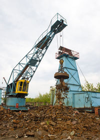 Crane at metallic junkyard against sky