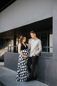 A young family is waiting for the baby and walks around the modern city. the husband looks 