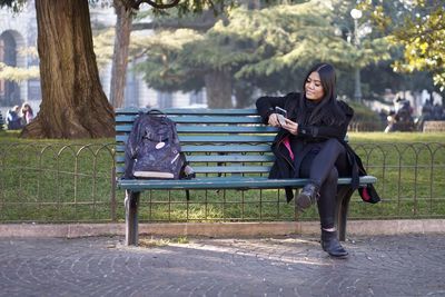 Woman using smartphone while sitting on bench at park