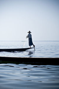 Rear view of man fishing on boat against blue sky
