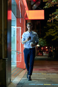 Young businessman walks with his smartphone and coffee cup at ni