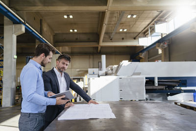 Businessmen with digital tablet and blue print standing at factory