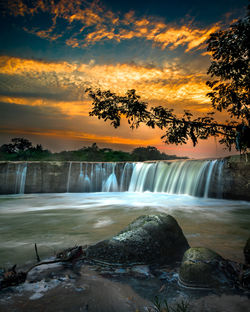 Scenic view of waterfall against sky during sunset