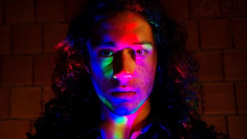 Portrait of young man standing against wall at night