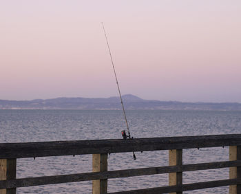 Fishing rod on pier over sea against sky during sunset