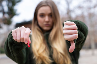 Close-up portrait of woman with pill showing thumbs down 