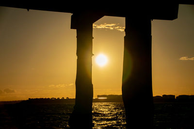 Silhouette built structure by sea against sky during sunset