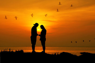 Silhouette people standing on shore against sky during sunset