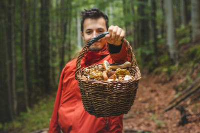 Man in outdoor clothing holds a basket full of mushrooms