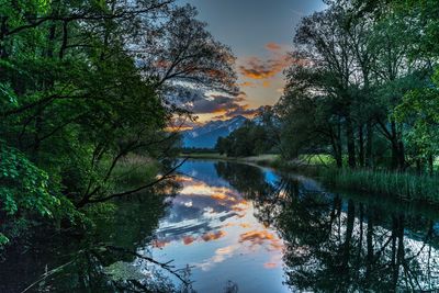 Scenic view of lake in forest against sky at sunset