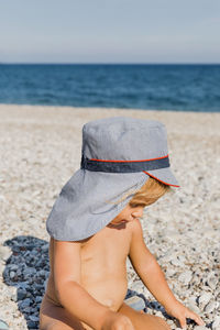 Shirtless girl in hat sitting at beach
