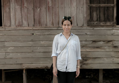 Portrait of mid adult woman standing by wooden house