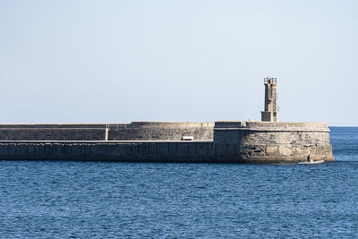 Lighthouse by sea against clear sky