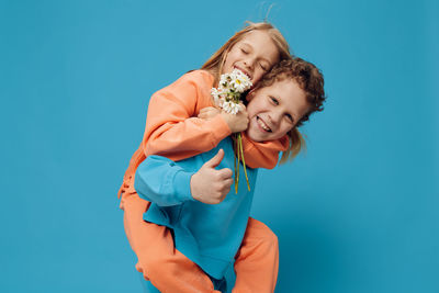 Portrait of brother carrying sister on back against blue background