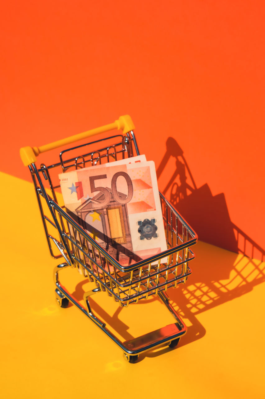 finance, currency, shopping cart, consumerism, shopping, colored background, wealth, business, retail, paper currency, buying, finance and economy, orange color, studio shot, no people, business finance and industry, investment, vehicle, indoors, savings, yellow