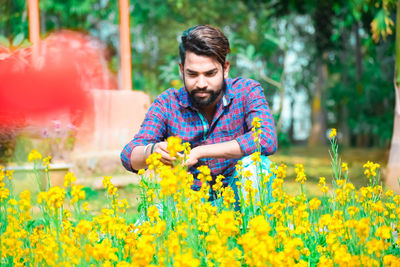 Portrait of man with yellow flowers on field