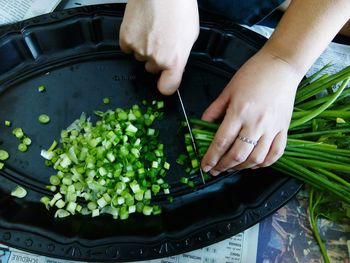 Cropped image of woman chopping spring onions in tray at home