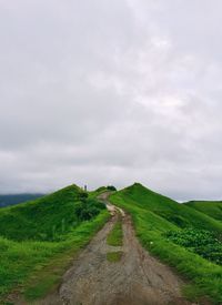 Dirt road amidst field against sky