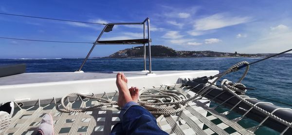 Low section of woman on sailboat at sea shore against sky