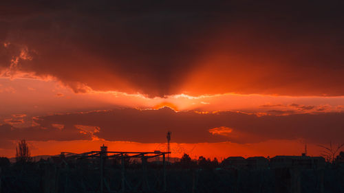 Silhouette of factory against dramatic sky during sunset