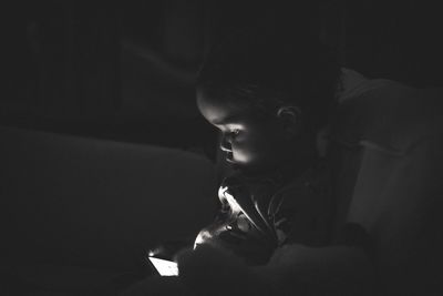 Baby boy using mobile phone while sitting on sofa in darkroom