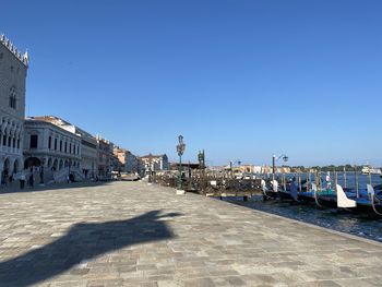 Canal passing through city against clear blue sky