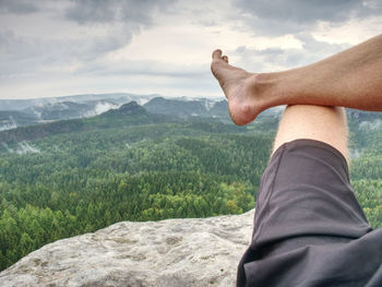 Midsection of man with hand on mountain against sky