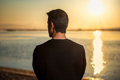 Rear view of man standing at beach during sunset