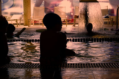 Rear view of silhouette boy standing at swimming pool