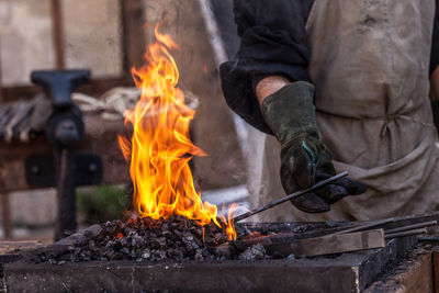 Midsection of man holding metal in bonfire at workshop