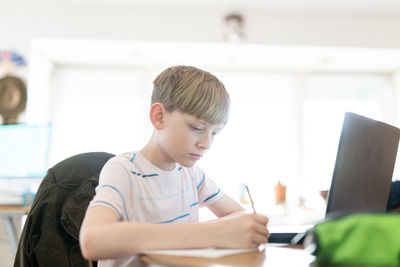 Tween writing notes while using laptop computer for homework