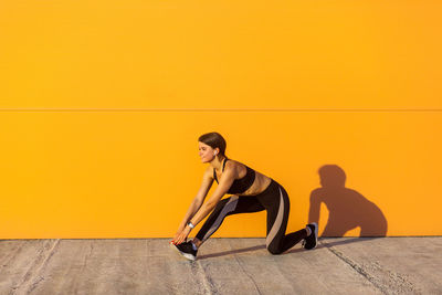 Full length of woman sitting on seat against yellow wall