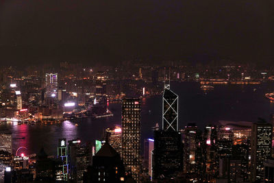 Illuminated city by river against sky at night